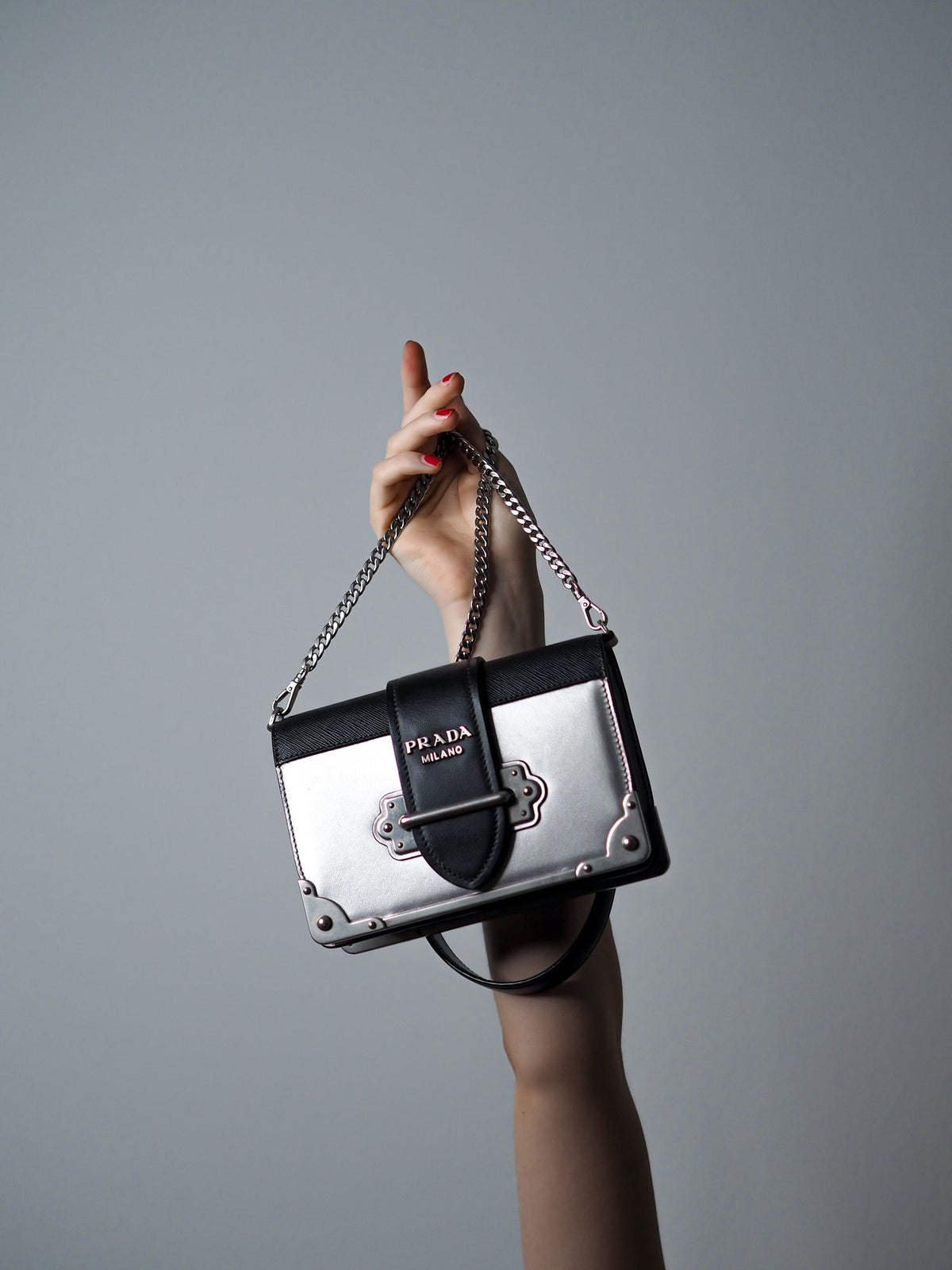 A hand holding a designer shoulder bag against a grey studio backdrop